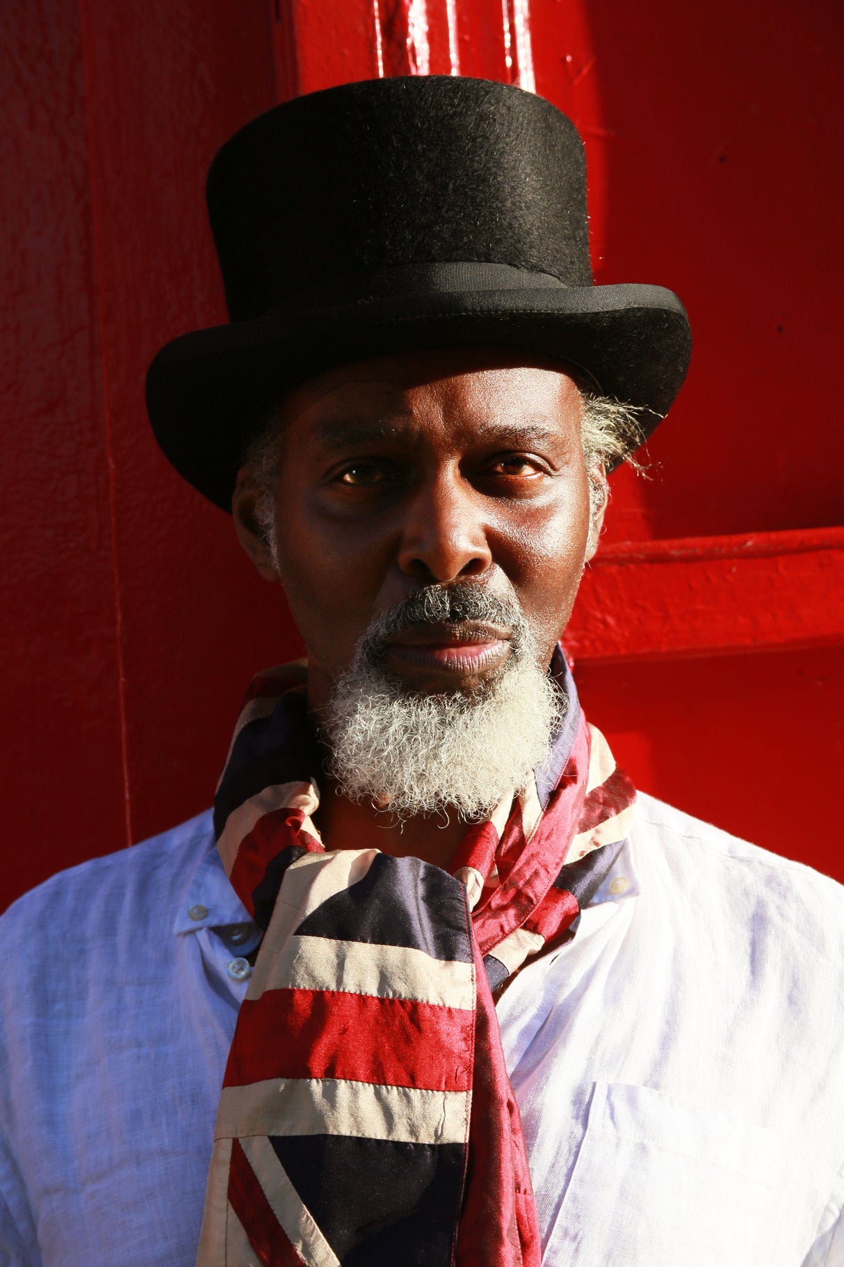 Man wearing a top hat and Union Jack silk scarf against a red background